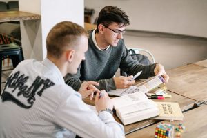 Home Two young men studying together, focusing on English grammar books in a modern indoor setting.