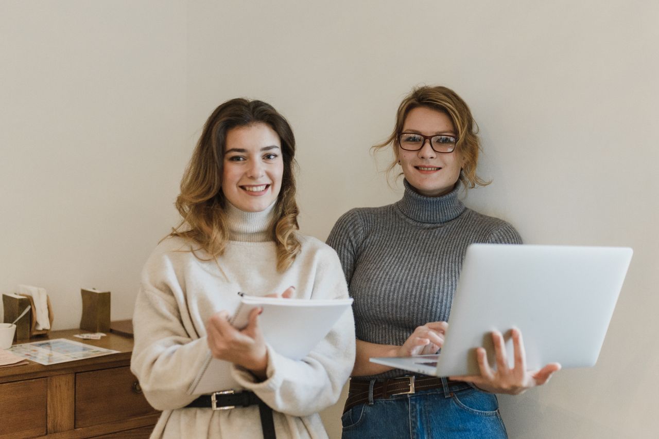 Services Smiling women collaborating with laptop and notebook in an office space.