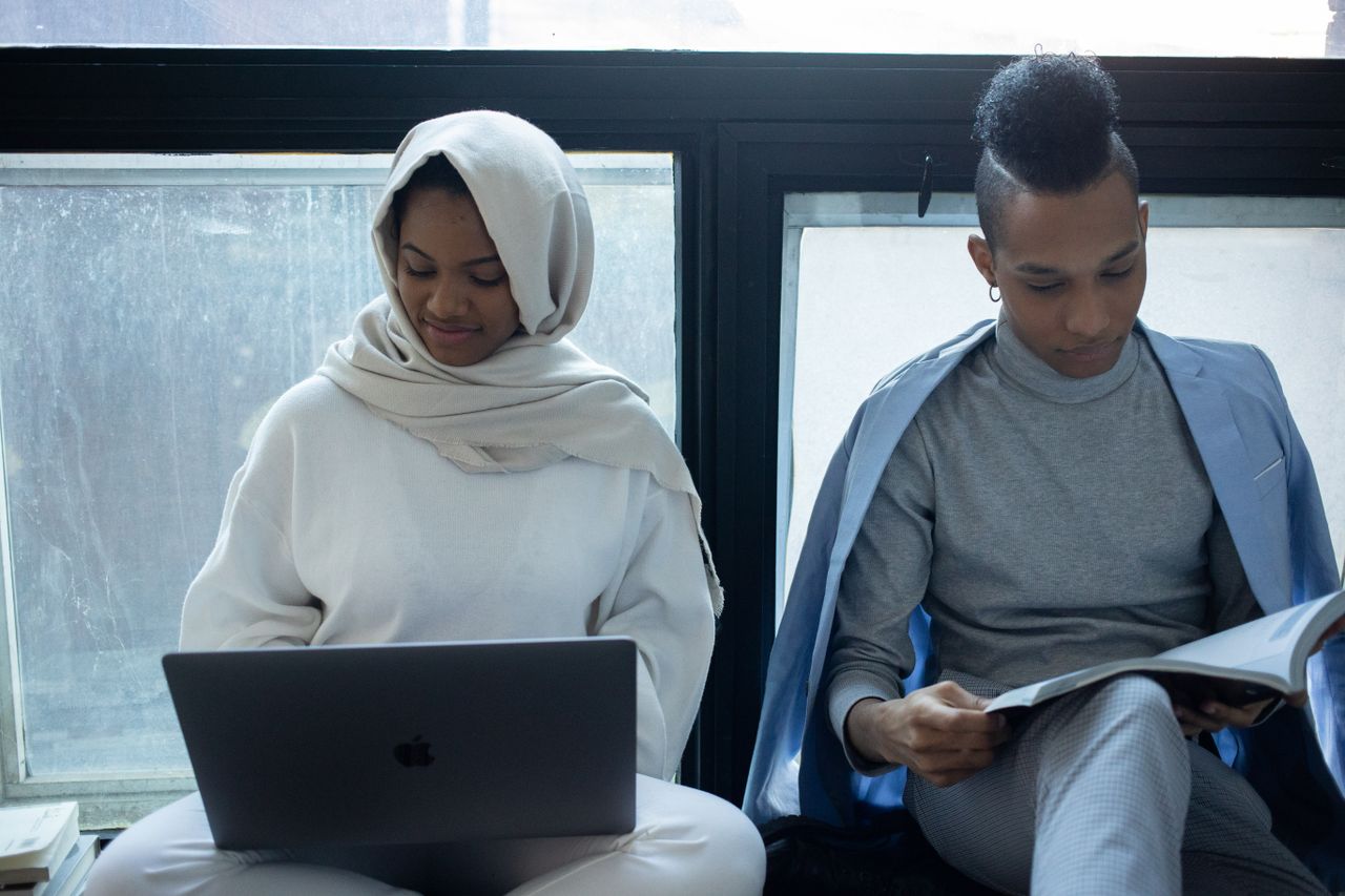 Services Concentrated African American woman in hijab working on laptop near classmate reading textbook during exam preparation